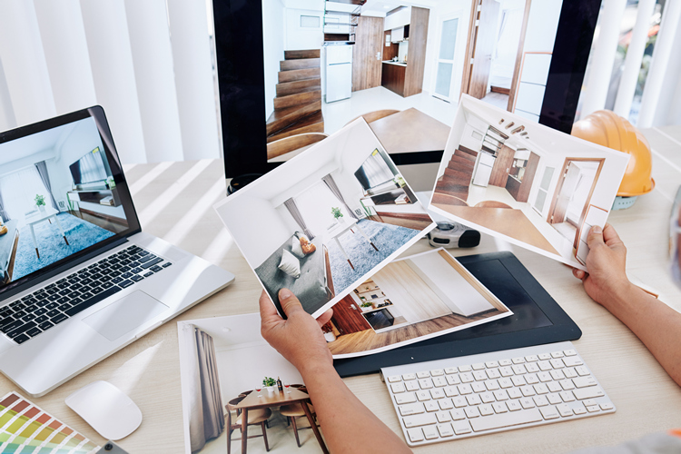 Interior designer sitting at desk and looking at printed photos of clients rooms after renovation