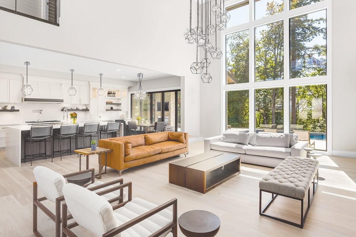 Beautiful living room interior in new luxury home with open concept floor plan. Shows kitchen, dining room, and wall of windows with amazing exterior view